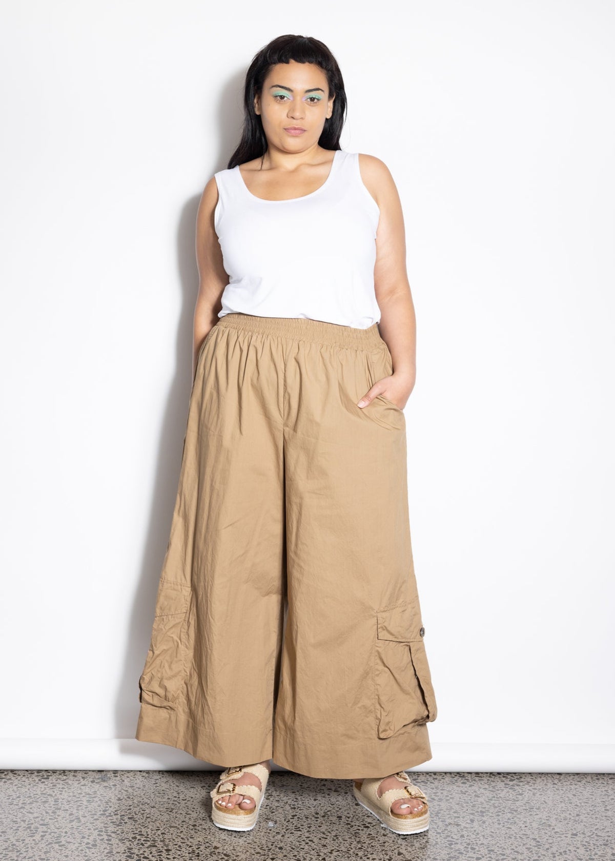 Woman wearing a white sleeveless top and beige wide-leg pants against a white background