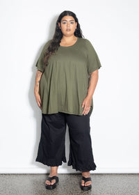 Woman wearing an olive green top and black pants against a white background