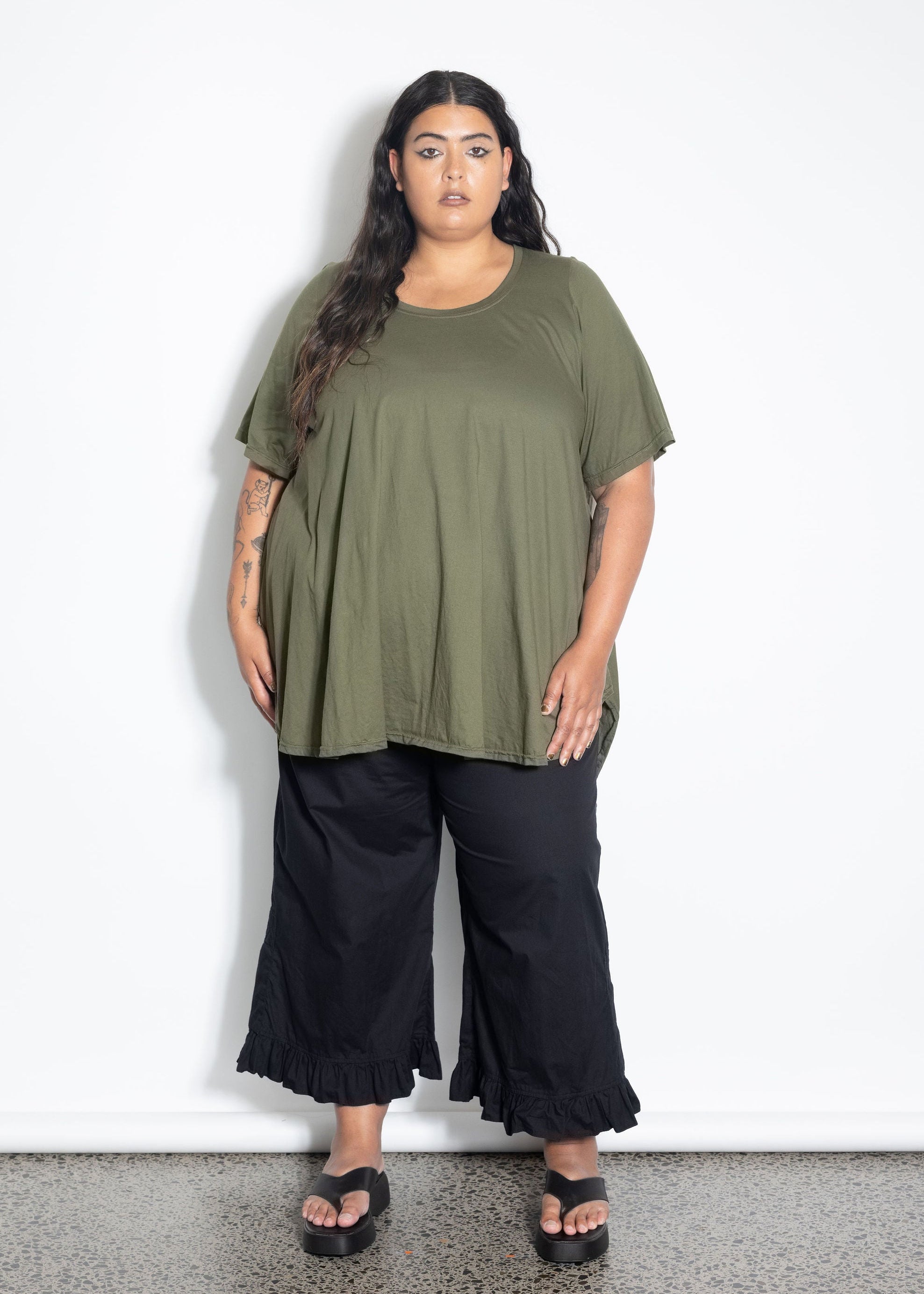 Woman wearing an olive green top and black pants against a white background