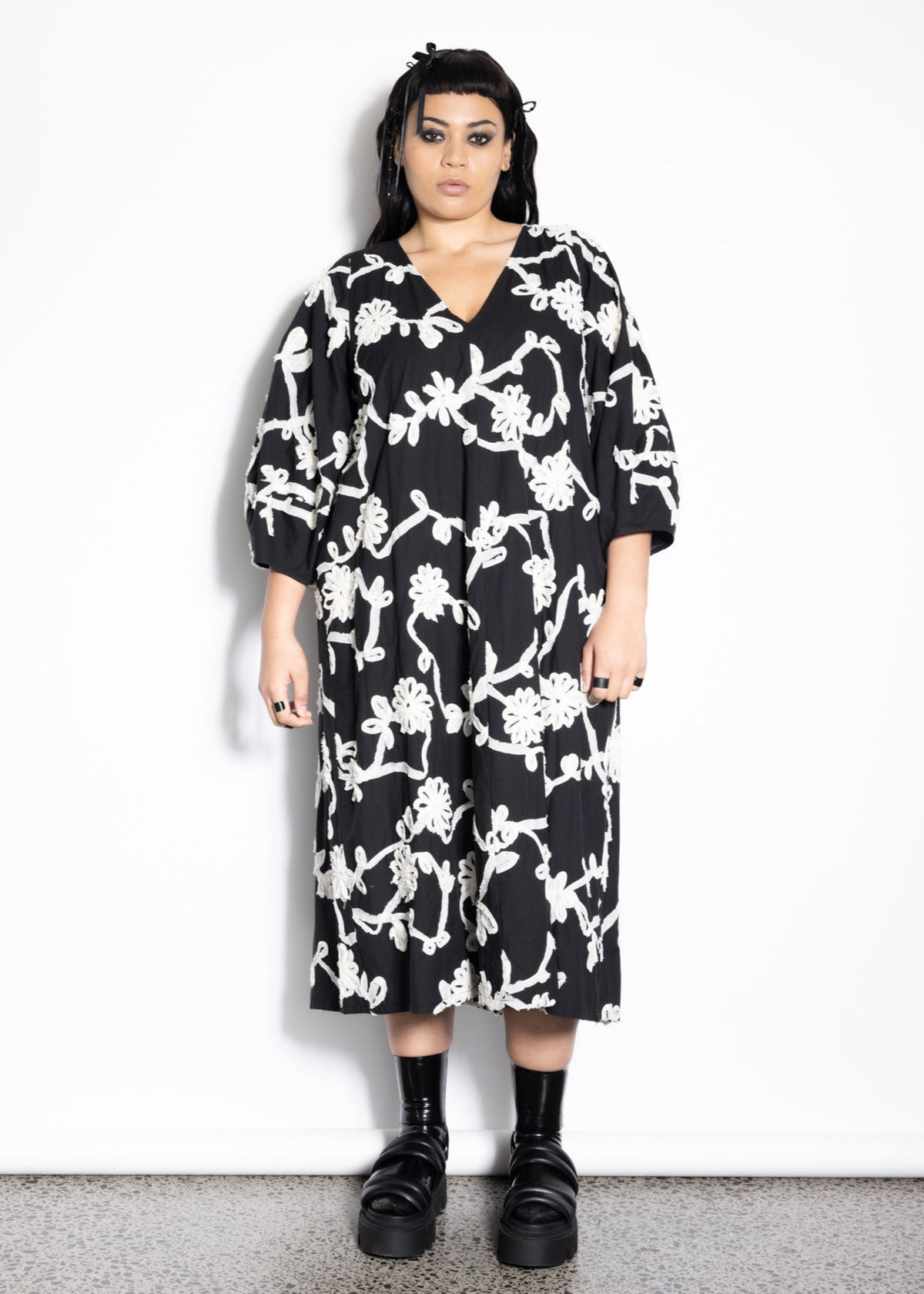 Person wearing a black floral dress against a white background
