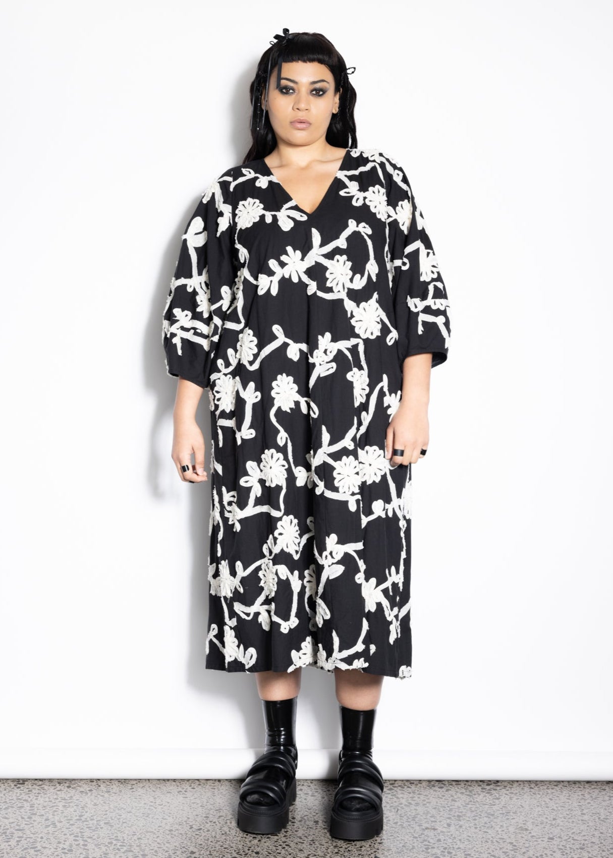 Person wearing a black floral dress against a white background
