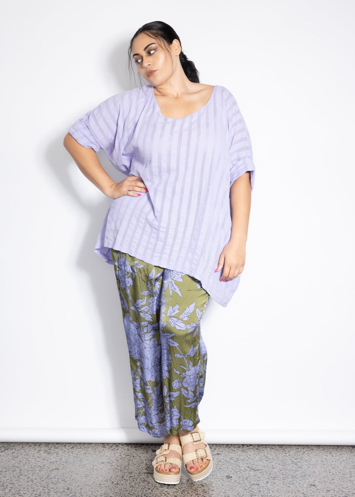 Woman wearing a light purple top and patterned pants on a white background